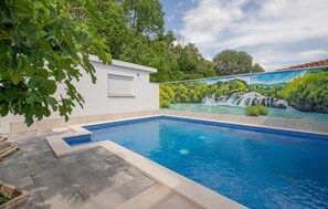 Une piscine dont le mur du fond est décoré d’une fresque représentant une cascade et de la végétation.