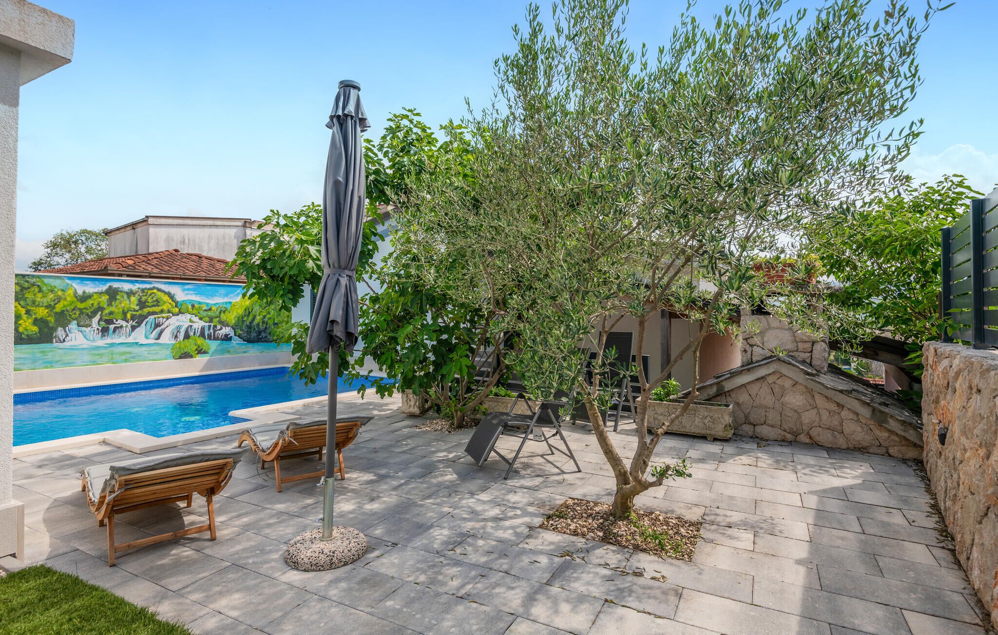 A swimming pool with a mural, outdoor seating, and a tree.