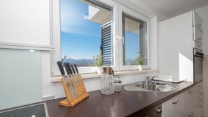 Een moderne keuken met een houten aanrecht, een roestvrijstalen spoelbak en uitzicht op bergen door het raam.