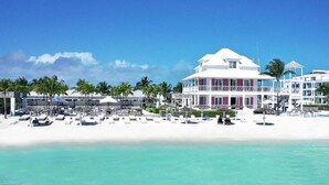 Un hôtel situé en bord de mer, avec une façade blanche, de nombreux balcons et une plage de sable équipée de chaises longues.