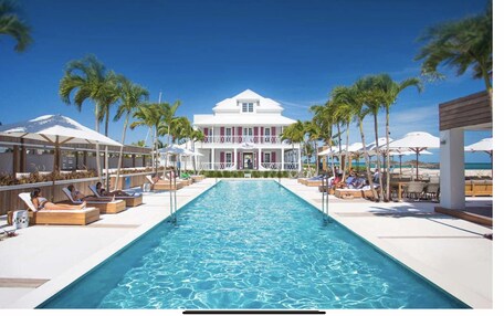 A poolside area with lounge chairs and umbrellas, a large pool, and a building with a white facade and red trim.
