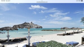 Une plage avec des parasols en chaume, des chaises longues et une promenade bordée de sable.