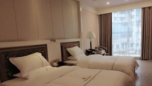 Een hotelkamer met twee bedden, een nachtkastje, een lamp en een groot raam met gordijnen.