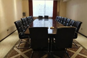 Een vergaderzaal met een lange tafel, zwarte stoelen en een vloerkleed.