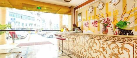 A hotel reception area with a marble counter, a clock, and a vase with flowers.