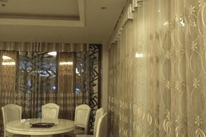 Un comedor con una mesa redonda y sillas, cortinas estampadas y un detalle decorativo en la pared.