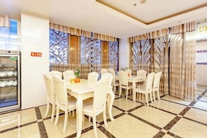 Un comedor de hotel con mesas y sillas blancas, un refrigerador y cortinas decorativas.