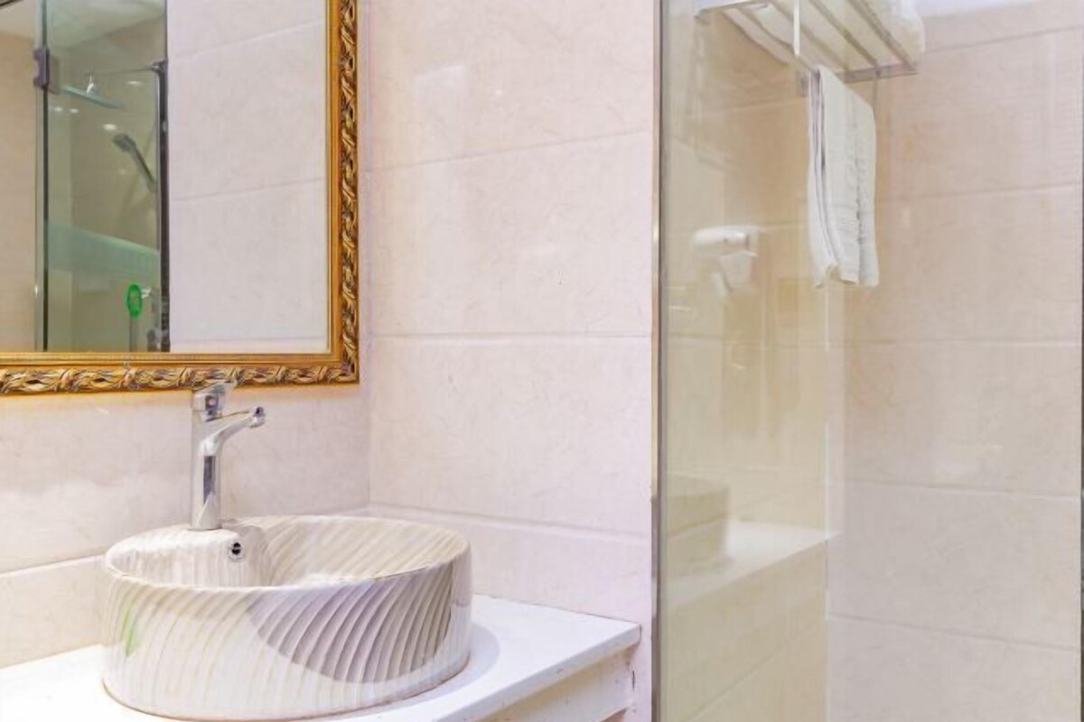 A bathroom with a round, ribbed sink, a gold-framed mirror, and a glass shower enclosure.