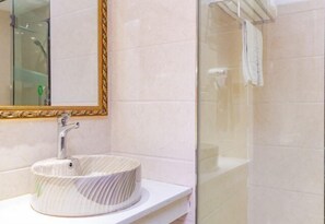 A bathroom with a round, ribbed sink, a gold-framed mirror, and a glass shower enclosure. - Sofie Grand Hotel (Wuchuan)