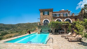 A stone building with a swimming pool, outdoor seating, and a view of the surrounding hills.