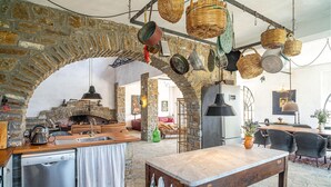 A rustic kitchen with stone walls, a wooden table, and hanging baskets.