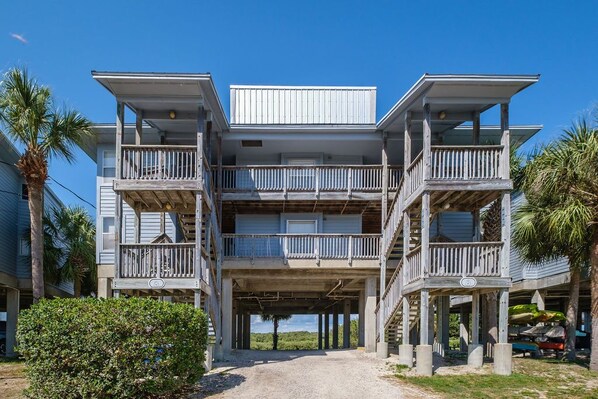 A multi-story beachfront building with balconies, a covered entrance, and a view of the ocean.