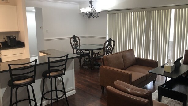 A modern living room with a brown leather sofa, a glass-top coffee table, and a dining area with a round table and chairs. - Beautifully furnished 1 Bedroom McLean Condo near Tysons corner (McLean)