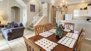 A dining area with a wooden table and chairs, a chandelier, and a staircase leading to another room.