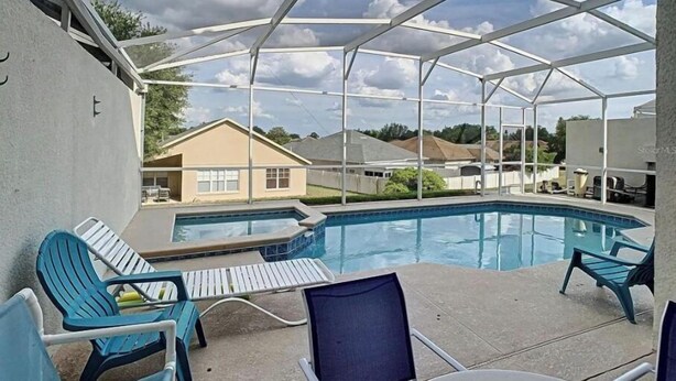 A covered outdoor swimming pool with lounge chairs and a table, surrounded by a metal frame structure.