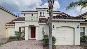 A two-story house with a red door, a garage, and a landscaped front yard.