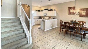 A spacious kitchen with white cabinets, a central island, and a dining area with wooden chairs and a table.