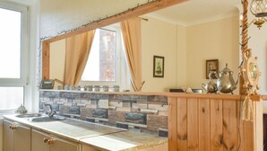 Une cuisine avec un pare-feu en pierre, des armoires en bois, un grand miroir et une fenêtre avec des rideaux.