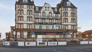 Un grand hôtel à plusieurs étages, de style architectural classique, doté d’un balcon central imposant et de nombreuses fenêtres.