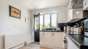 A modern kitchen with white cabinets, a black countertop, and a window with blinds. - Tanglin Farm - Wonky Donkey (Brinkworth)