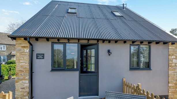 A cottage with a metal roof, a door, and two wicker chairs outside. - Tanglin Farm - Wonky Donkey (Brinkworth)