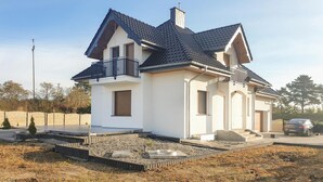Ein zweistöckiges Haus mit einem dunklen Ziegeldach, einem Balkon im oberen Geschoss und einer kleinen Veranda.