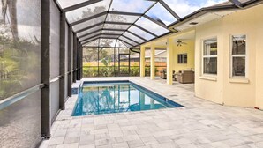 A covered swimming pool with a glass ceiling, surrounded by a tiled patio and a yellow wall.