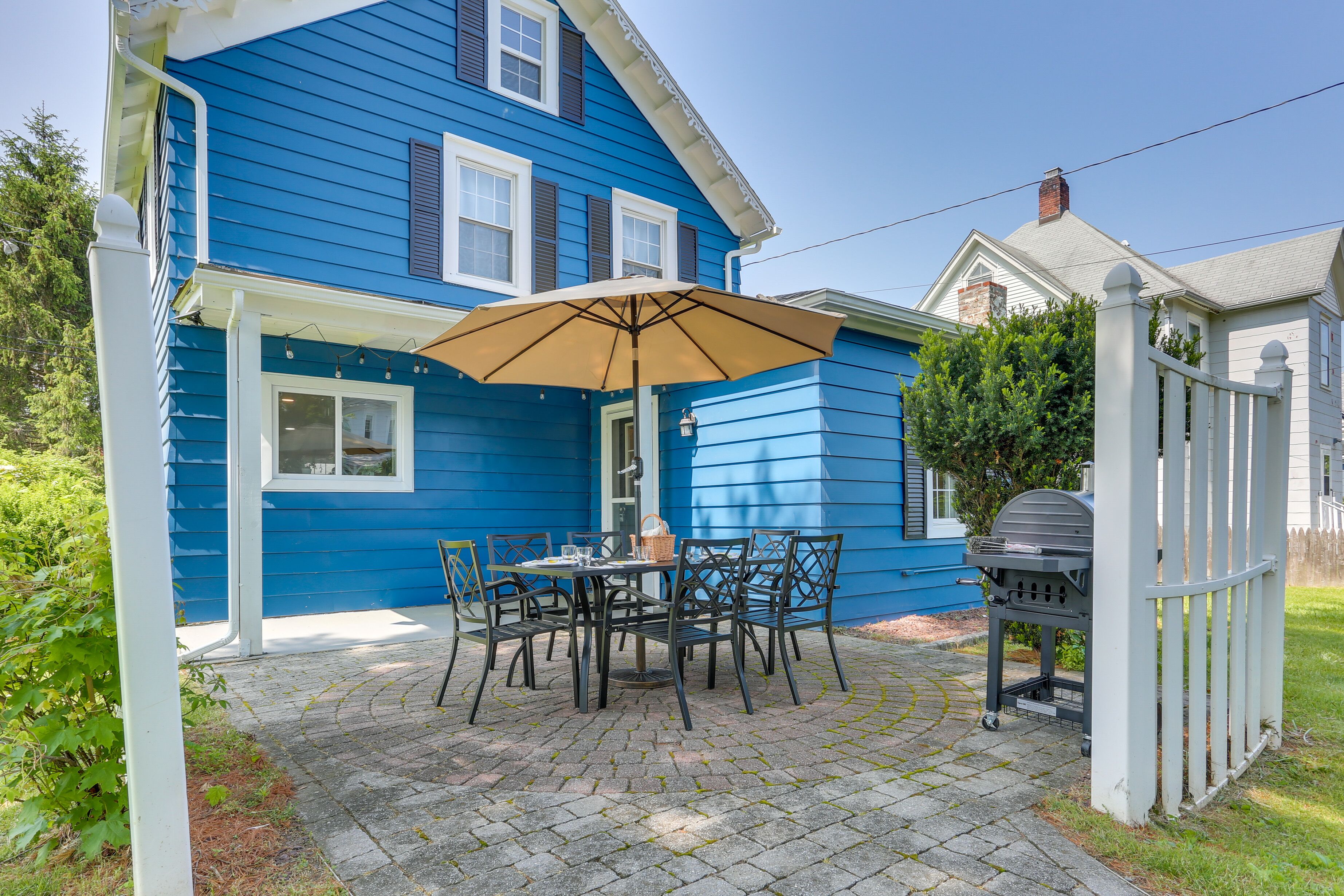 Casa azul con un patio que incluye una mesa, sillas y una parrilla.