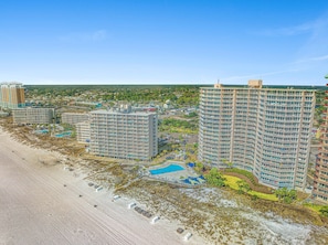 Un grand hôtel avec de nombreux étages, une piscine et un espace aménagé sur la plage.