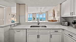 A modern kitchen with white cabinets, a stainless steel sink, and a view of the ocean through large windows.