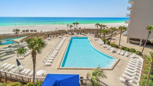 A swimming pool with lounge chairs and palm trees, overlooking a beach and ocean.