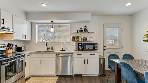 A modern kitchen with white cabinets, stainless steel appliances, and a wooden dining table with blue chairs.