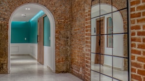 Un pasillo con paredes de ladrillo, un espejo arqueado grande y una pared verde azulado al final.