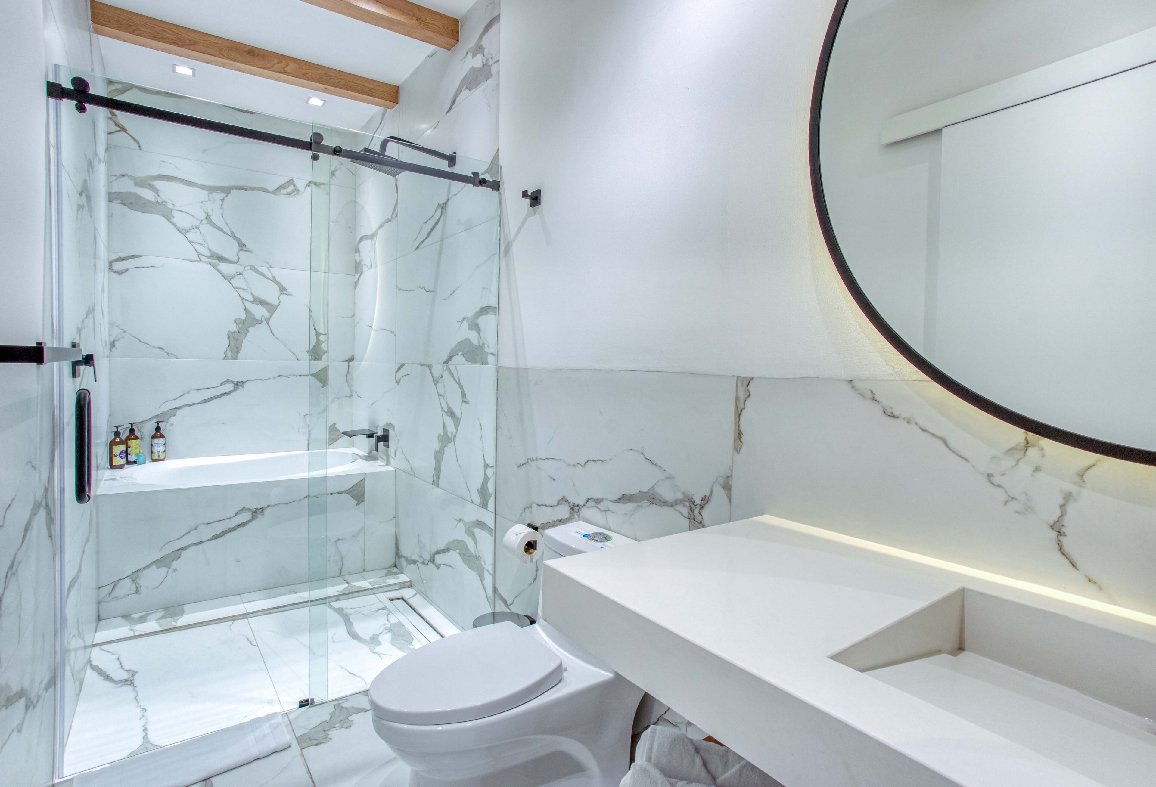 A modern bathroom with a glass-enclosed shower, a white toilet, and a marble-tiled wall.