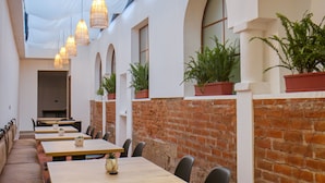 Un comedor amplio con mesas y sillas, pared de ladrillo y lámparas colgantes.