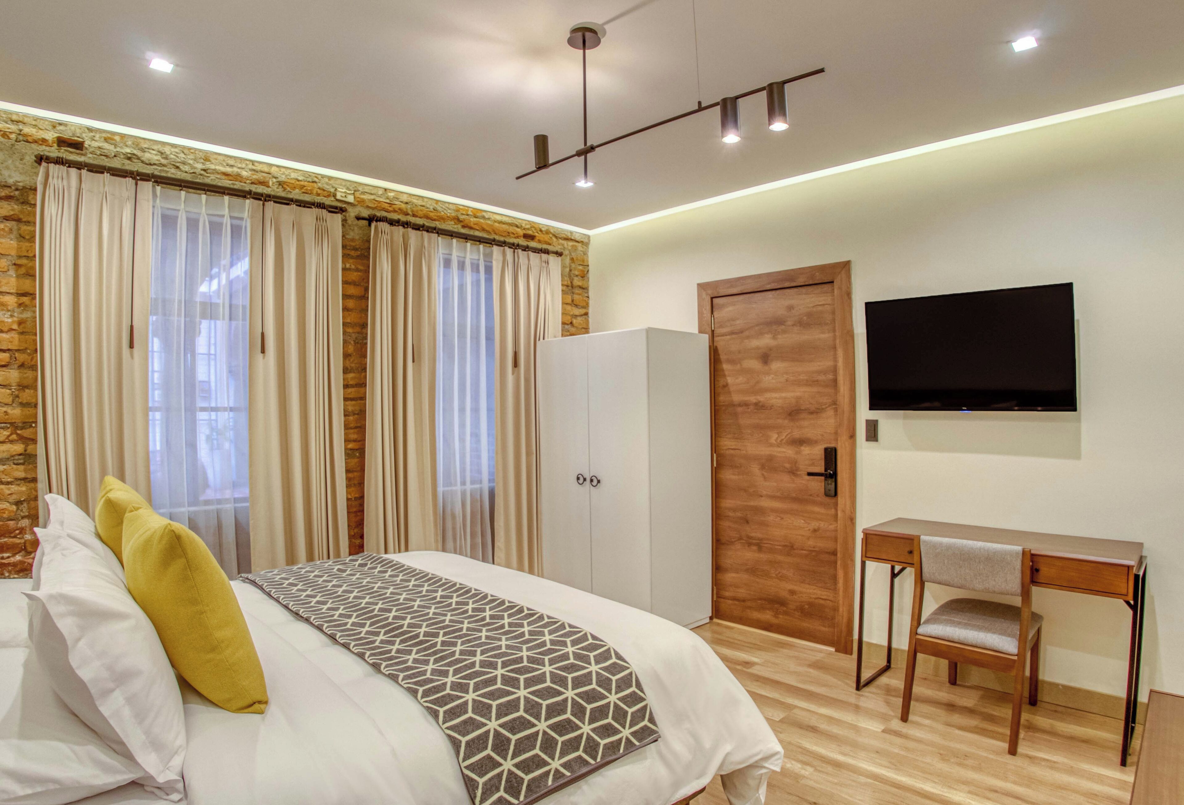 A bedroom with a bed, a desk, a chair, a wardrobe, and a TV.