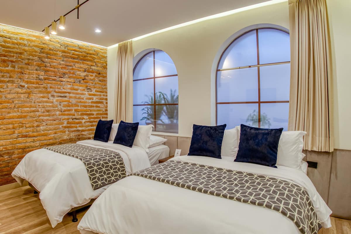 Une chambre d’hôtel avec deux lits, un mur en briques, de grandes fenêtres en arc de cercle et un plancher en bois.