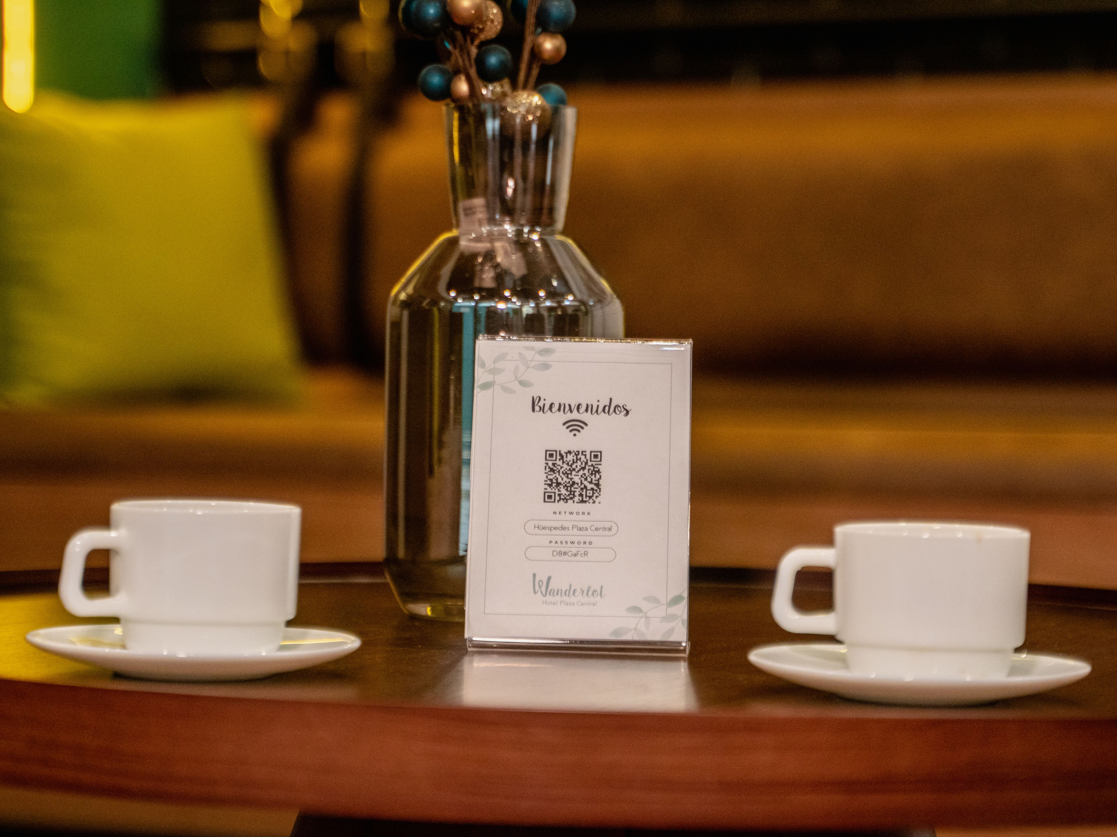 A table with a QR code sign, two white cups, and a vase with blue and gold ornaments.