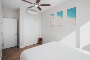 A bedroom with a bed, a ceiling fan, a white door, and three beach-themed wall art pieces.