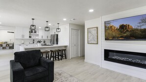 A modern living room with a black sofa, a fireplace, and a large TV mounted on the wall. - Riverfront Ranch, Near Wine Tasting & Sedona (Cottonwood)