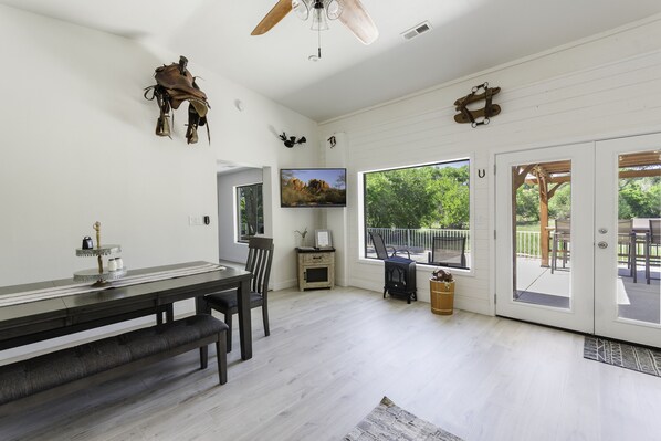 A spacious room with a dining table, chairs, a television, and a large window offering a view of the outdoors. - Riverfront Ranch, Near Wine Tasting & Sedona (Cottonwood)
