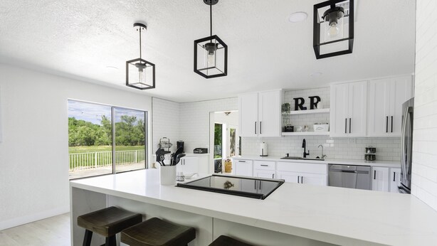 A modern kitchen with white cabinets, a large island with stools, pendant lights, and a view of greenery outside. - Riverfront Ranch, Near Wine Tasting & Sedona (Cottonwood)
