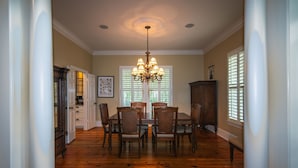 A dining area with a wooden table and chairs, a chandelier, and a window with blinds.