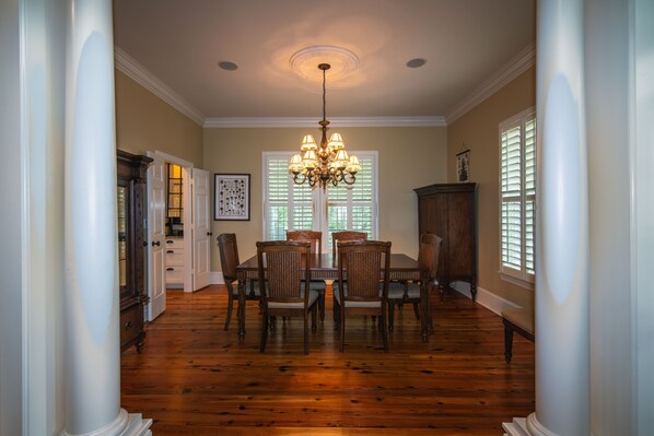 A dining area with a wooden table and chairs, a chandelier, and a window with blinds.