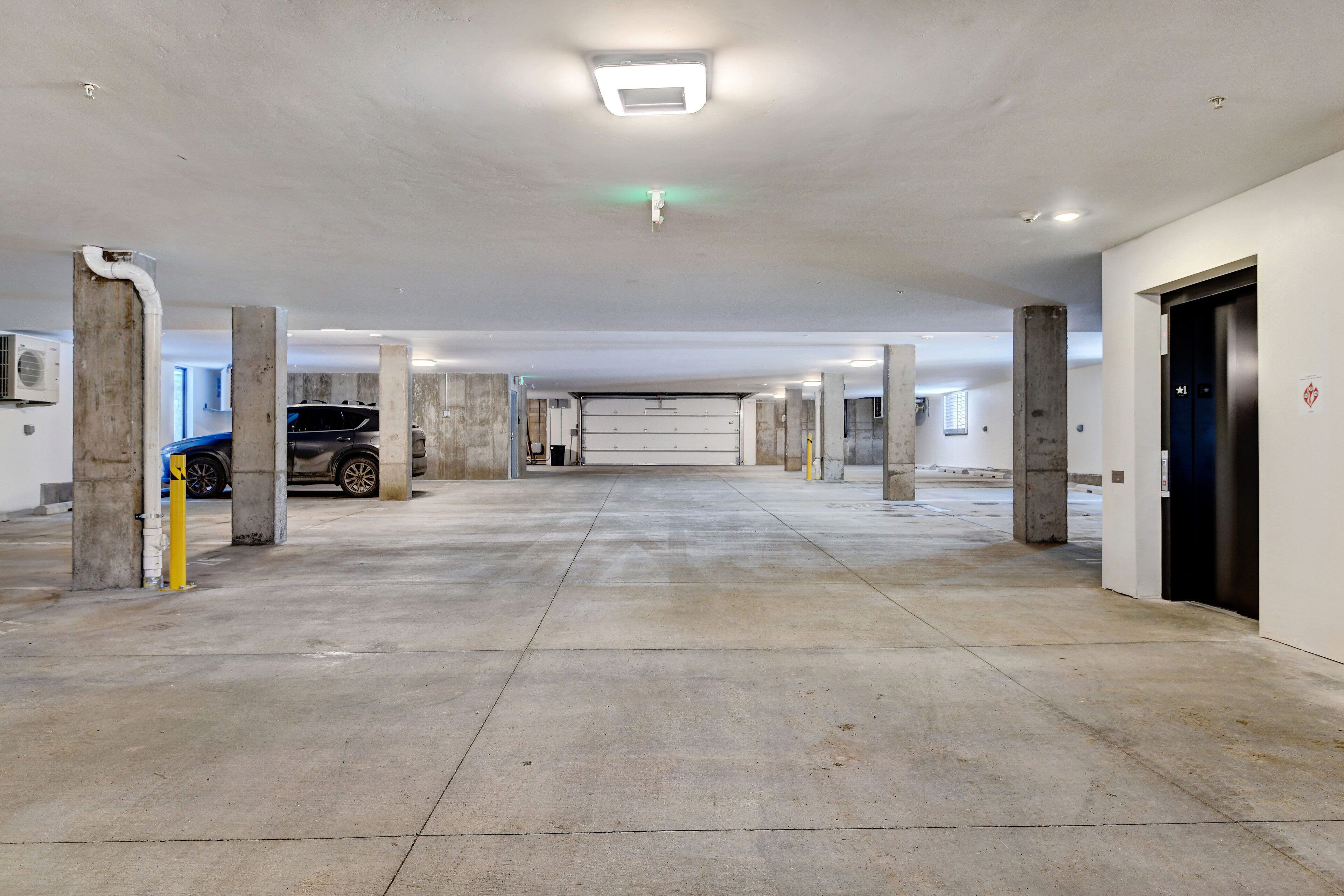 A parking garage with concrete pillars, a central walkway, and a car parked on the left.