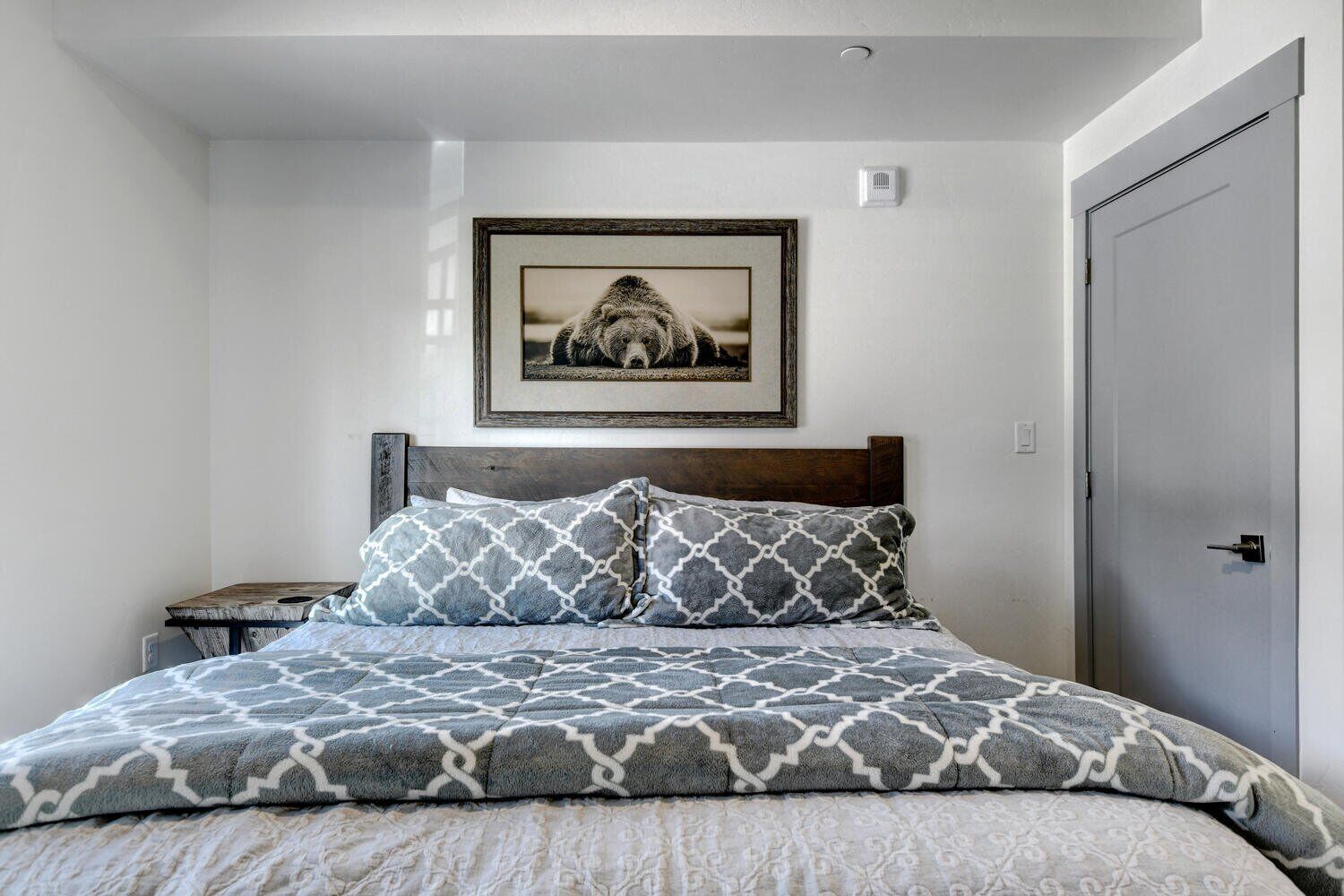 A bedroom with a bed, a nightstand, a framed picture on the wall, and a door.