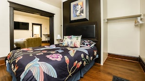 Een hotelkamer met een groot bed, een hoofdeinde, een schilderij boven het bed, een deur naar een andere kamer, en een houten vloer.