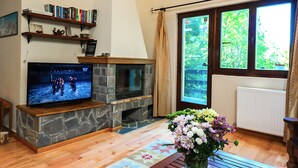 A living room with a stone fireplace, television, bookshelves, and a large window with a view of greenery. - Mountain Family Chalet (Comarnic)
