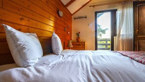 A wooden-paneled room with a bed, a nightstand, a lamp, and a window with curtains. - Mountain Family Chalet (Comarnic)
