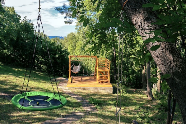 A wooden swing set and a green trampoline in a grassy area with trees. - Mountain Family Chalet (Comarnic)
